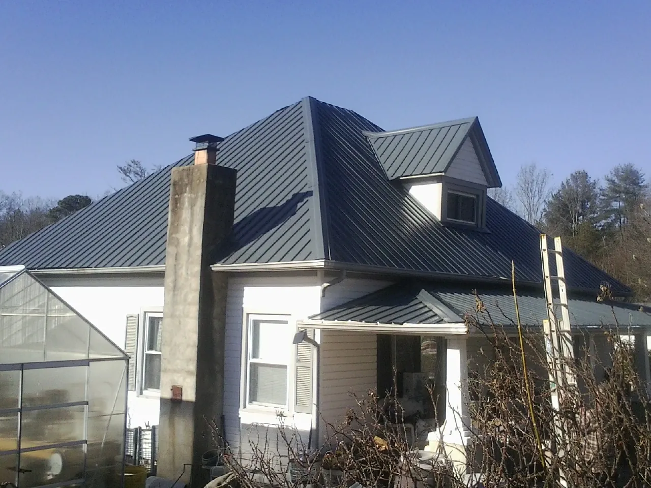 Dark blue standing seam metal roof on a white farmhouse with dormer — Slate & Tile Roof Repair by Roofing Brothers in Garfield