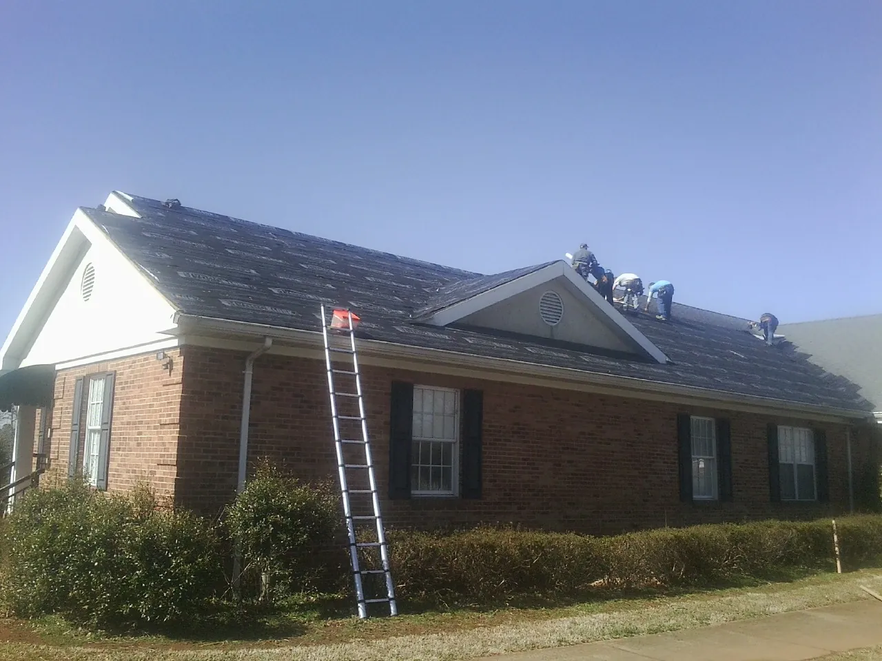Crew tearing shingles off a brick ranch roof with a ladder set — Emergency Roof Repair work by our crew in Garfield