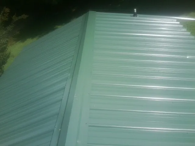 New green metal panels meeting at the ridge of a roof — Flat Roof Repair work by our crew in Garfield