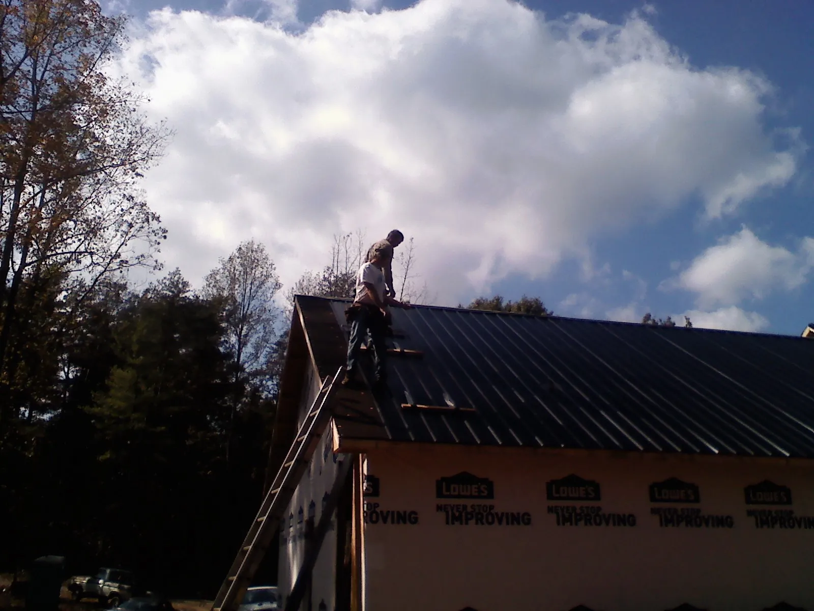 Roofer fastening dark metal panels high against a cloudy sky, from a Roof Inspection job in Garfield
